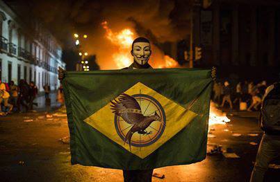 Manifestante exibe bandeira brasileira com o símbolo da saga Jogos Vorazes no centro, em protestos no Brasil