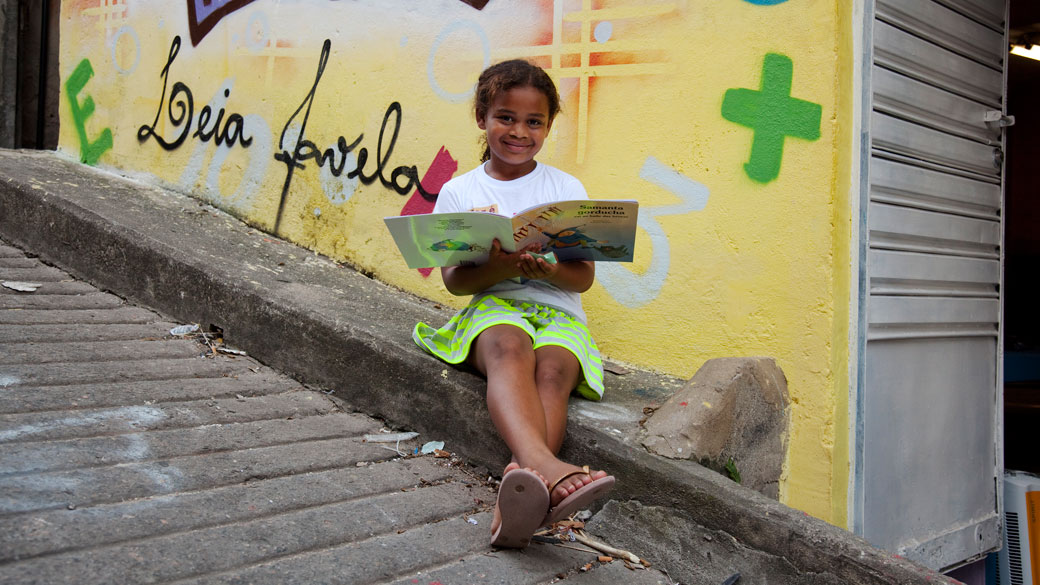 Gabriely Vitória Soares Estêvão, 8 anos, em frente ao ponto de leitura do projeto Ler é Dez Leia Favela Caracol, complexo da Penha, no Rio de Janeiro