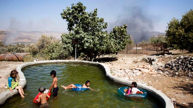 Enquanto crianças judaicas se divertem em uma piscina, é possível ver ao fundo a fumaça proveniente do conflito entre colonos israelenses e palestinos, próximo a um assentamento judaico na Cisjordânia. Nesta segunda, autoridades israelenses demoliram duas estruturas em West Bank, na Cisjordânia