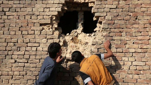 Afegãos olham um buraco na parede de uma casa causado por um foguete de ataque em Cabul