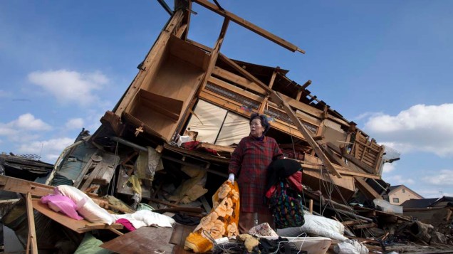 Aiko Musashi se surpreende ao olhar a destruição da casa de seu vizinho enquanto recolhe seus pertences pessoais na cidade de Kesennuma, Japão
