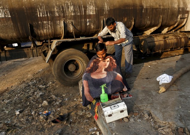 Barbeiro ambulante corta o cabelo de um caminhoneiro ao lado de seu caminhão em uma área industrial de Mumbai, na Índia