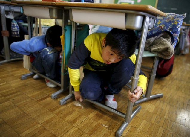 Crianças em idade escolar se protegem embaixo de mesas durante um exercício de simulação de terremoto em uma escola de Tóquio, no Japão, para marcar o aniversário do terremoto e tsunami de 2011 que matou milhares de pessoas e desencadeou uma crise nuclear