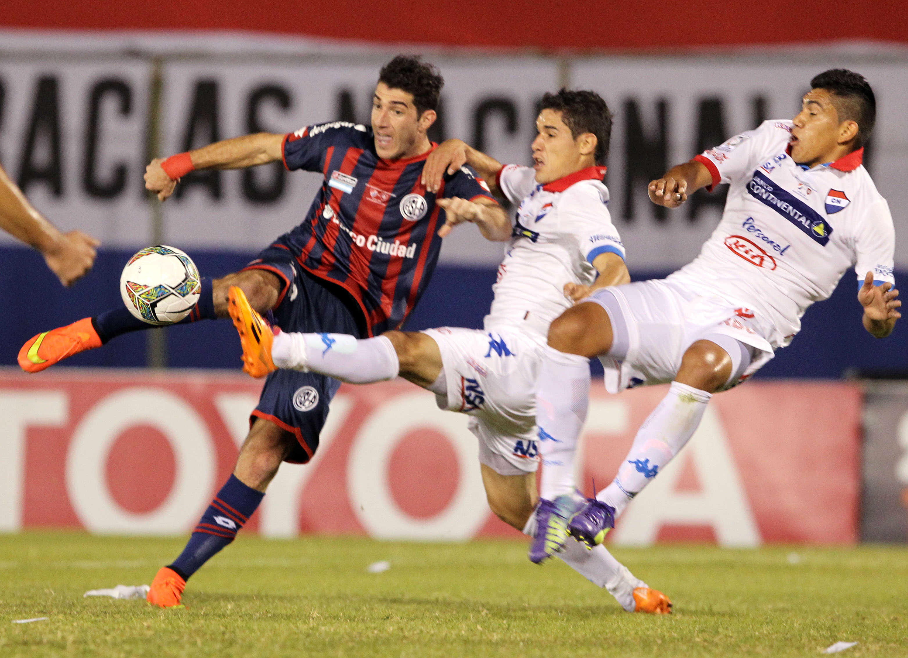 Mauro Matos, do San Lorenzo , disputa a bola com Silvio Torales e Raúl Píris, do Nacional