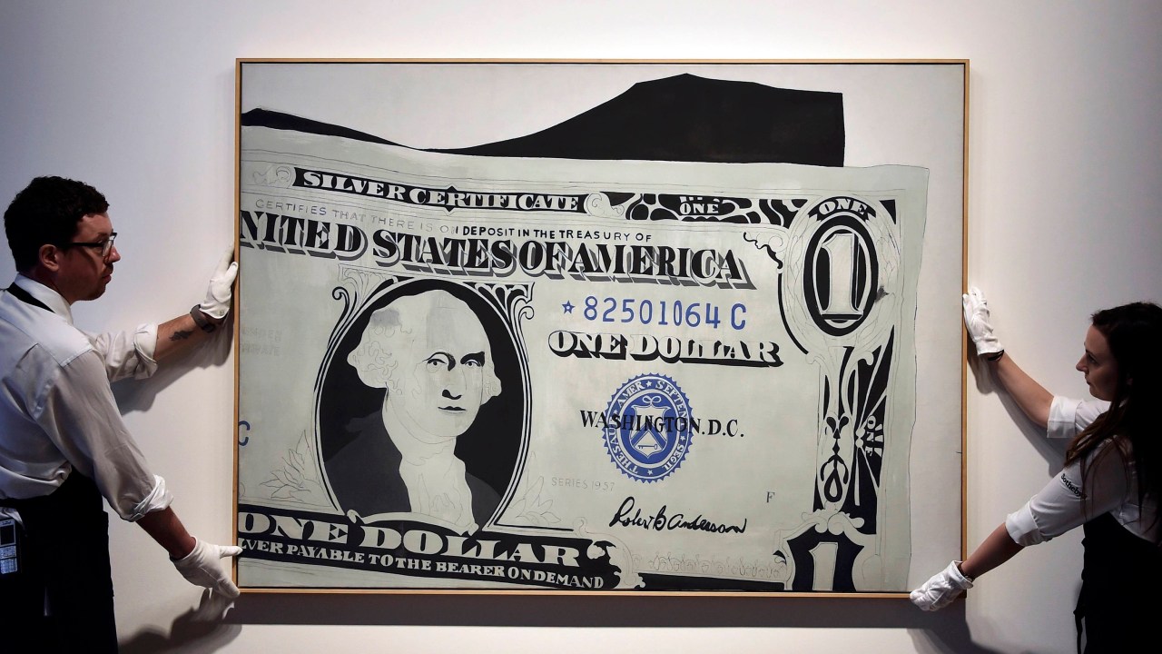 Funcionários posam com o quadro "Silver Certificate", de Andy Warhol, na casa de leilões Sotheby, em Londres