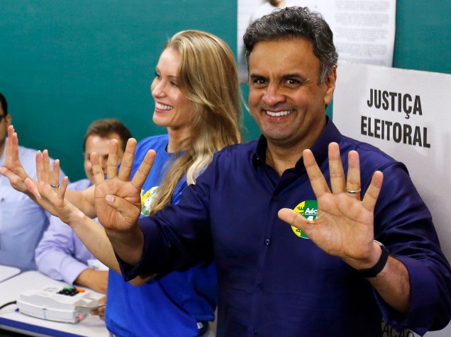 O candidato presidencial Aécio Neves e sua esposa, Leticia Weber, fazem gestos para os fotógrafos durante votação do segundo turno, em Belo Horizonte, Minas Gerais