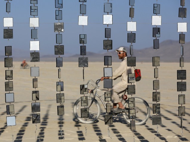Homem passa de bibicleta por uma instalação artística durante o "Burning Man 2015 - Carnaval de Espelhos", festival de música e arte que acontece no deserto de Black Rock, Nevada. Cerca de 70.000 pessoas de todo o mundo se reúnem para passar a semana no deserto durante o festival