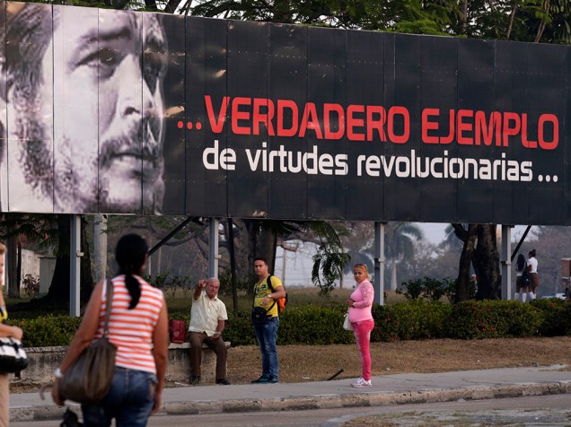 Pessoas passam por grande mural que homenageia o herói cubano Ernesto "Che" Guevara. O outdoor diz "Verdadeiro exemplo de vitudes revolucionárias"