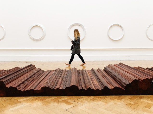 Mulher passa diante das obras Cama (primeiro plano) e Sem Título (no fundo) do artista chinês Ai Weiwei em exposição na Royal Academy of Arts em Londres
