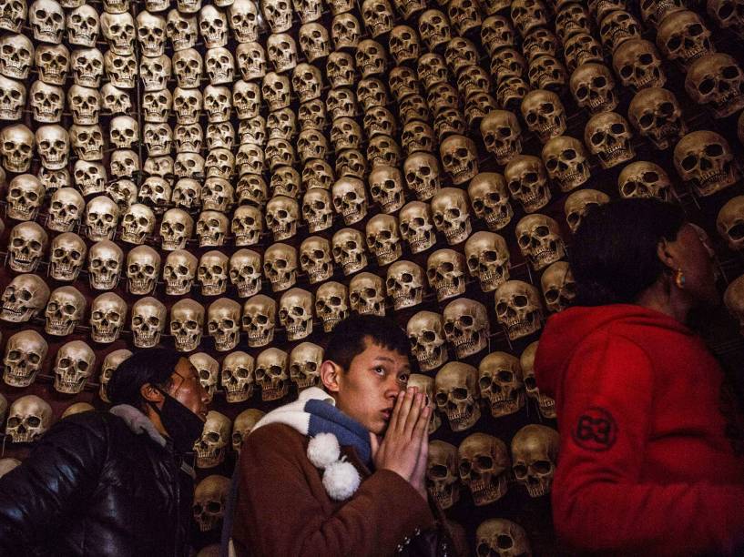 Devotos tibetanos observam crânios humanos falsos colocados dentro de uma sala no local utilizado para enterros em Larung, na China