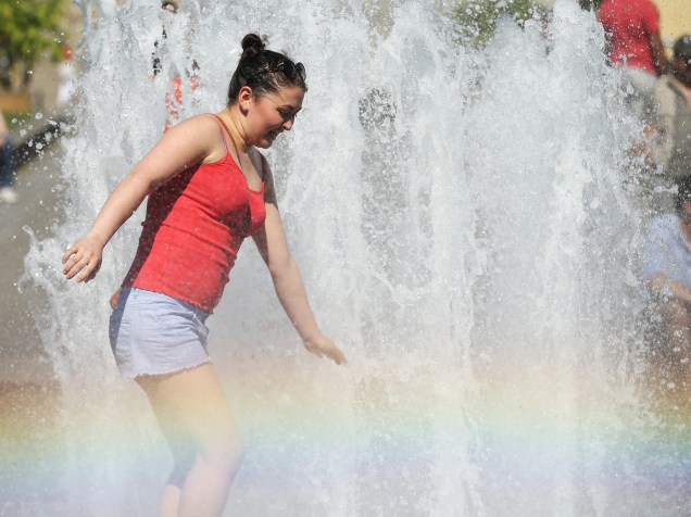 Mulher se refresca em uma fonte pública, enquanto o spray de água cria um arco-íris no centro de Berlim, na Alemanha - 02/07/2015