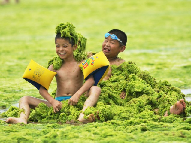 Em Qingdao, província de Shandong, China, garotos brincam em uma praia coberta por algas verdes