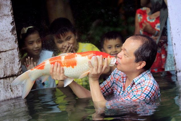 Dono de um zoológico de Malabon, Manny Tangco, beija uma carpa japonesa koi enquanto crianças observam a apresentação da nova atração do local, chamada de O mundo das kois, no norte da região metropolitana de Manila, nas Filipinas