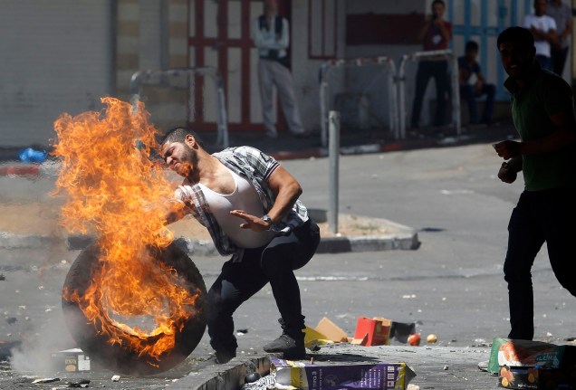 Homem empurra pneu em chamas durante protesto em Hebron, na Cisjordânia, contra a ofensiva israelense em Gaza