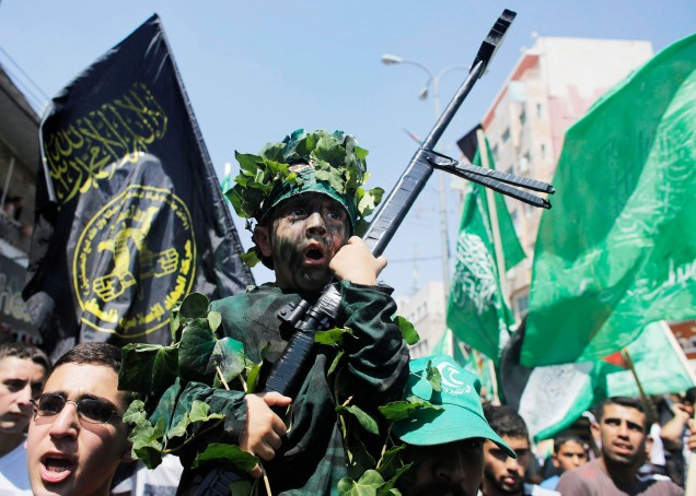 Menino vestido com trajes militares, segura a réplica de um fuzil durante um comício comemorando mais um anúncio do cessar-fogo, considerado pelos palestinos como uma vitória sobre Israel, na cidade de Hebron Menino vestido com trajes militares, segura a réplica de um fuzil durante um comício comemorando mais um anúncio do cessar-fogo, considerado pelos palestinos como uma vitória sobre Israel, na cidade de Hebron