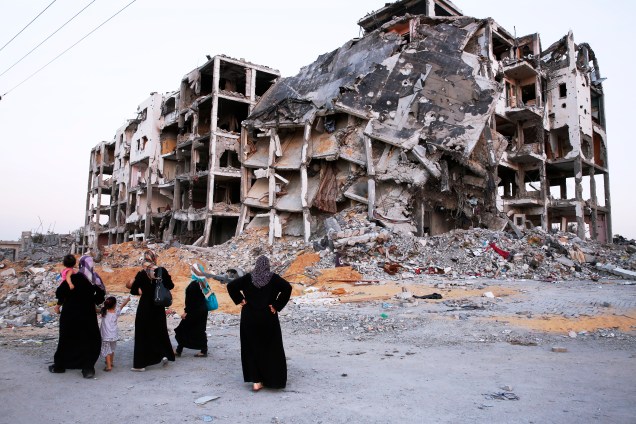 Mulheres e crianças palestinas são vistas próximo aos destroços de um complexo de edifícios destruídos pelos combates entre militantes do Hamas e o Estado de Israel, ao norte da Faixa de Gaza Mulheres e crianças palestinas são vistas próximo aos destroços de um complexo de edifícios destruídos pelos combates entre militantes do Hamas e o Estado de Israel, ao norte da Faixa de Gaza
