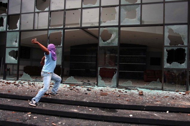 Um jóvem encapuzado joga pedras em frente ao Congresso do Estado de Guerrero durante protesto, no México