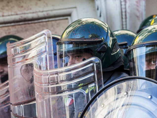 Agentes da polícia italiana, se protegem do ataque de manisfestantes que jogam ovos e fogos de artifício durante um protesto em frente ao edifício do Ministério da Economia, em Roma - 14/11/2014