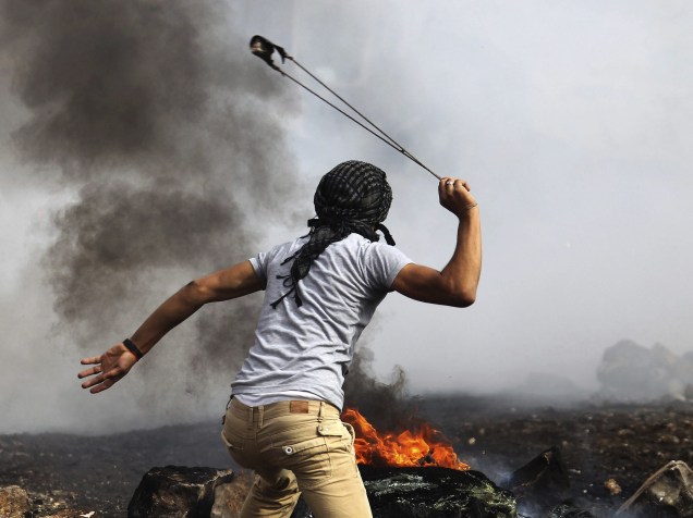 Manifestante palestino usa seu estilingue para atirar uma bomba de gás lacrimogêneo disparada por soldados israelenses durante confrontos nos arredores do assentamento judaico de Kedumim, perto da cidade de Nablus, na Cisjordânia - 14/11/2014