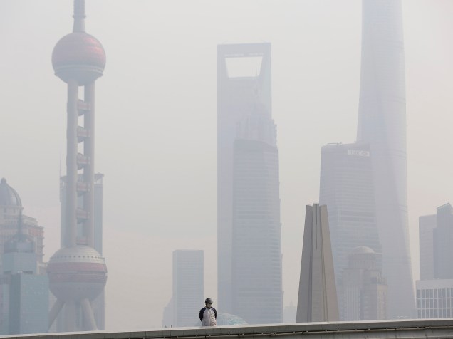 Homem usa uma máscara para se proteger da poluição, em uma ponte em frente ao distrito financeiro de Pudong, em Xangai, na China