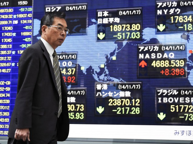 Pedestre passa por uma tela mostrando índices do mercado de ações de diferentes países, em Tóquio. O Japão entrou em recessão técnica após uma contração do PIB no trimestre de julho a setembro, segundo dados oficiais