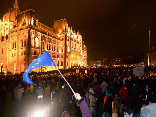 Na Hungria, manifestantes seguram faixas e bandeiras durante comício do Dia da Indignação, em frente ao parlamento de Budapeste. Dezenas de pessoas se reuniram em todo o país nesta segunda-feira (17) como demonstração de insatisfação com as políticas do atual governo de direita liderado pelo primeiro-ministro Viktor Orban
