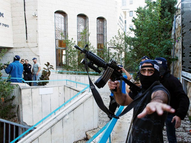 Policial israelense segura uma arma perto da cena de um ataque em que dois suspeitos palestinos armados com machados e facas mataram quatro pessoas em uma sinagoga de Jerusalém