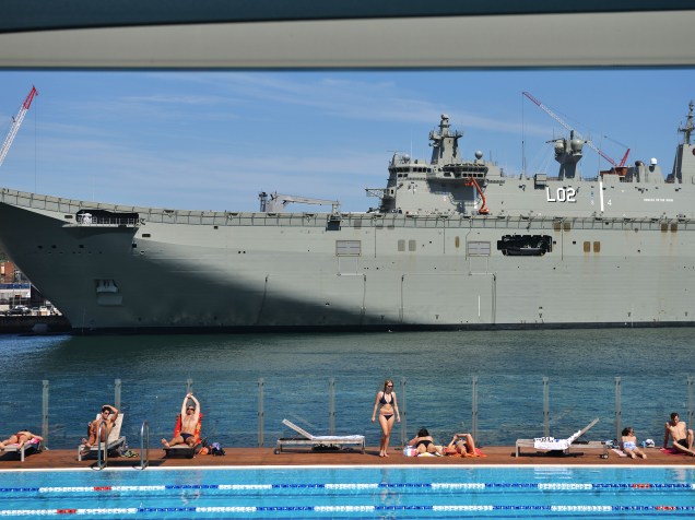 Pessoas tomaram banho de sol em uma piscina em frente ao HMAS Canberra, o mais recente navio de guerra da marinha de guerra australiana, atracado no Garden Island Naval em Sydney