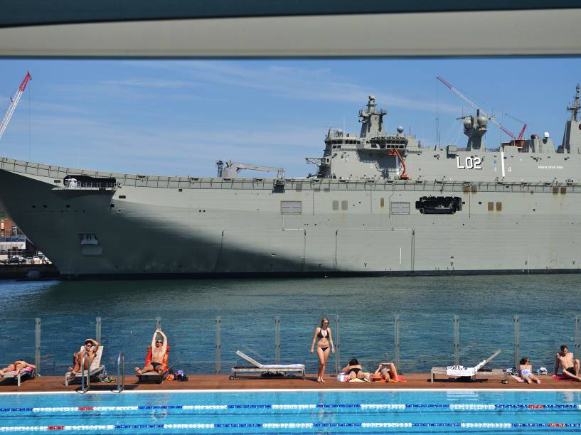 Pessoas tomam banho de sol em uma piscina em frente ao HMAS Canberra, o mais recente navio de guerra da marinha de guerra australiana, atracado no Garden Island Naval em Sydney - 21/11/2014