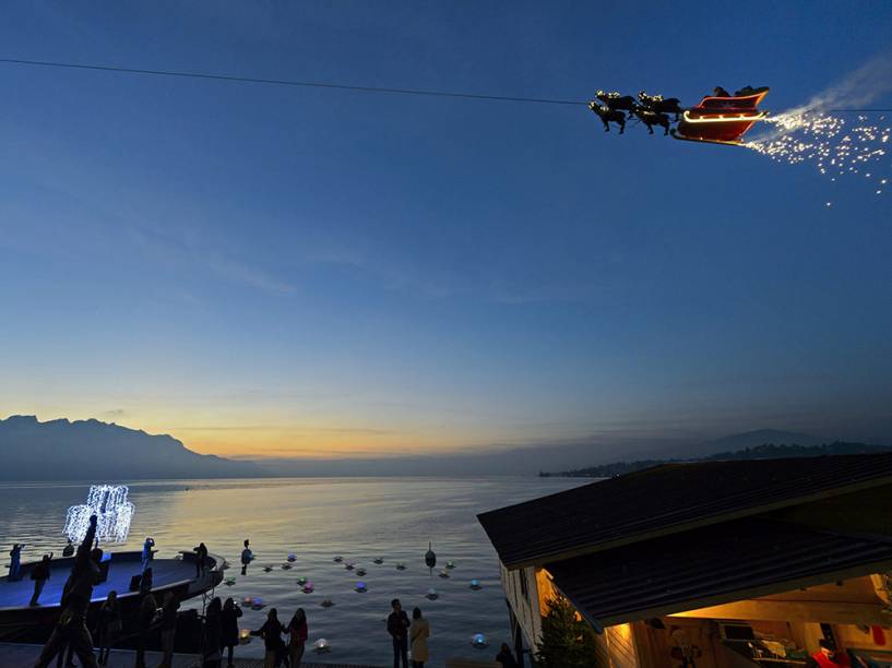 Um homem vestido de Papai Noel cumprimenta as pessoas de seu trenó conduzido por renas, no Lago de Genebra, durante o pôr-do-sol em Montreux, na Suíça