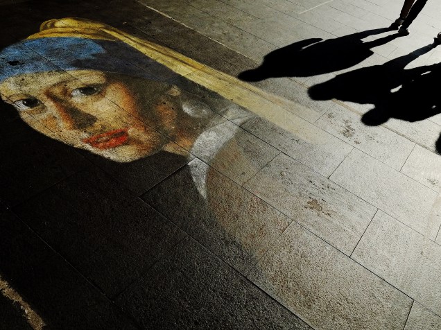 Pedestres caminham sobre um desenho que que reproduz a obra Moça com Brinco de Pérola, de Vermeer, no centro de Roma