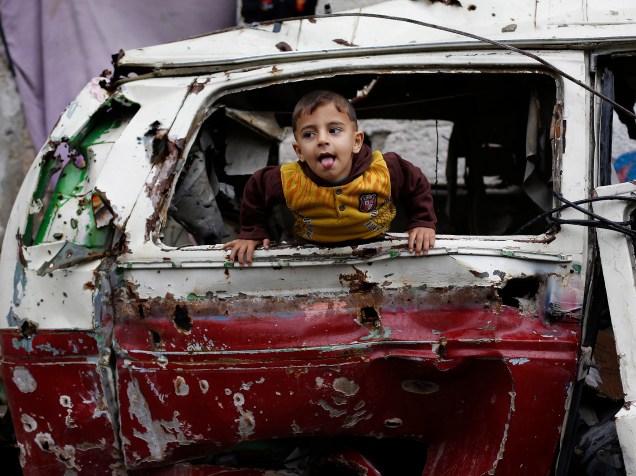 Menino palestino brinca dentro dos destroços de um carro, próximo a casas destruídas durante os conflitos entre Israel e militantes do Hamas, na região da Faixa de Gaza 