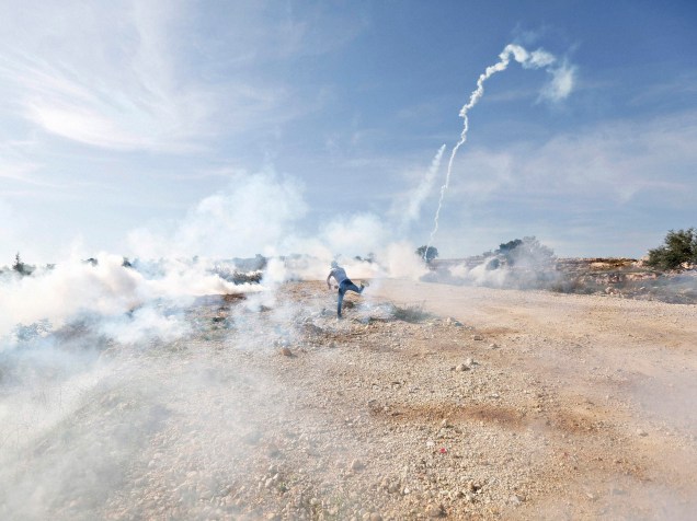 Manifestante palestino lança de volta uma bomba de gás lacrimogêneo disparada por soldados israelenses durante confrontos após uma manifestação contra os assentamentos judaicos na Cisjordânia, na aldeia de Bilin, perto de Ramallah - 05/12/2014