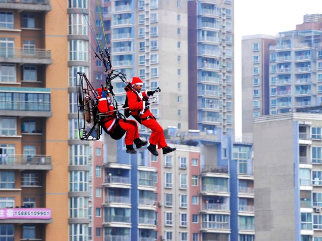 Homens fantasiados de Papai Noel voam com um paramotor voam próximos aos edifícios da cidade de Guiyang, na China, durante evento de comemoração do Natal