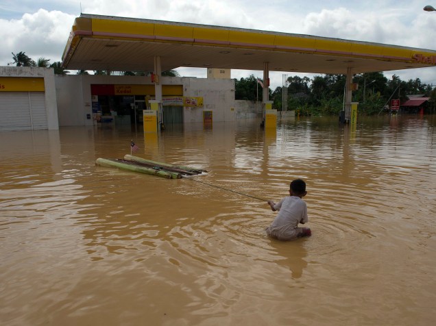 Menino brinca próximo a um posto de gasolina coberto por água em Kota Bharu, na Malásia. O país enfrenta uma grave enchente que obrigou mais de 100 mil pessoas a deixarem suas casas