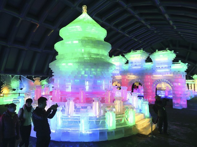 Algumas pessoas tiram fotografias de esculturas de gelo iluminadas com luzes coloridas durante um festival em Pequim, na China