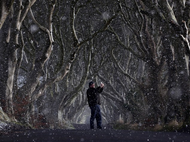 Na Irlanda do Norte, homem tira foto em meio a floresta enquanto neva na cidade de Antrim. O cenário ficou famoso após as gravações da série Guerra dos Tronos