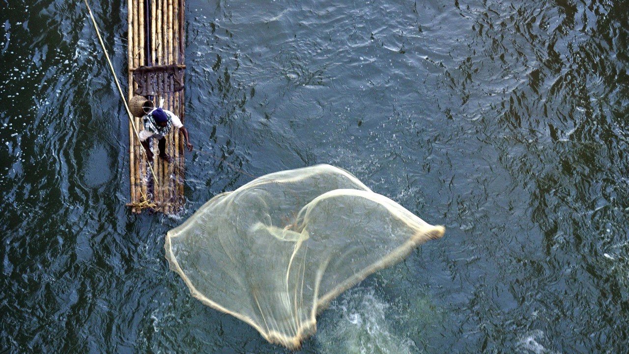 Pescador indiano lança rede de balsa de bambu no rio Howra, em Chakmaghat, no extremo leste do país, próximo à fronteira com Bangladesh
