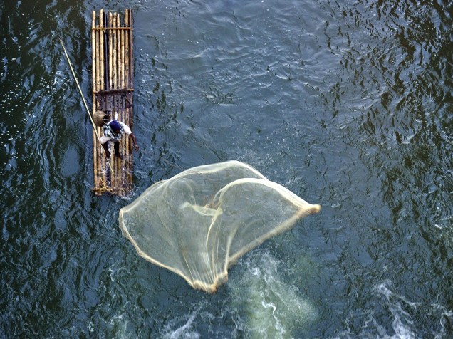 Pescador indiano lança rede de balsa de bambu no rio Howra, em Chakmaghat, no extremo leste do país, próximo à fronteira com Bangladesh