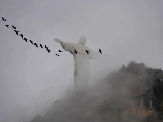 Em meio à neblina, pássaros sobrevoam o Cristo Redentor, na zona sul do Rio de Janeiro, na manhã desta sexta-feira (23). Segundo a previsão do tempo, o dia seguirá nublado com pancadas de chuva a qualquer hora e máxima de 31 graus