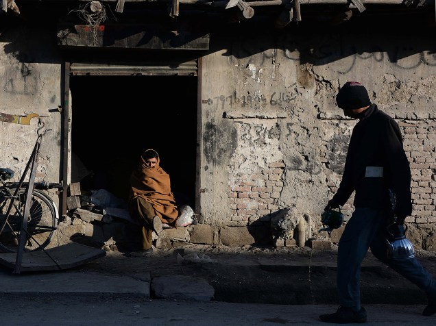 Vendedor observa homem passar em frente à sua casa na cidade de Jalalabad, no Afeganistão