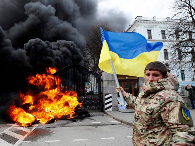 Combatente do batalhão Aydar balança bandeira ucraniana em frente ao Ministério de Defesa da Ucrânia, onde, momentos antes, foi ateado fogo, em Kiev