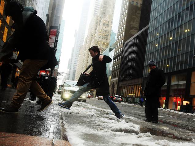 Homem pula possa de gelo para alcançar a calçada após tempestade de gelo que atingiu o bairro de Manhattan, em Nova York