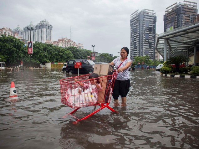 Mãe usa um carrinho de compras para o transporte de sua filha e de seus mantimentos em um estacionamento de um shopping em Kelapa Gading, Indonésia. As fortes chuvas tem causando inundações em muitas partes da capital do país