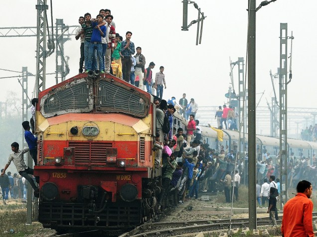 Passageiros viajam pendurados e sobre um trem que sai de uma estação nos arredores de Nova Délhi, na Índia - 25/02/2015