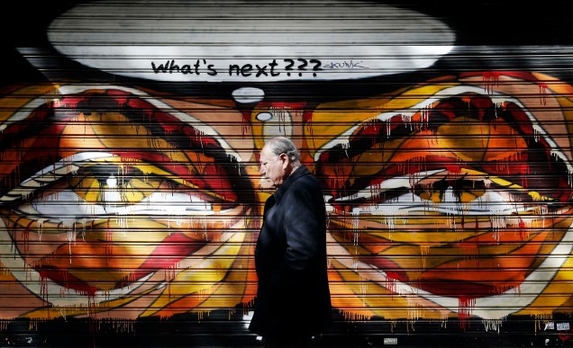 Homem caminha ao lado de um grafite em Antenas, na Grécia - 25/02/2015