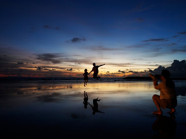 Mulher tira foto de seu marido e filho durante o pôr do sol na praia de Kuta, na Indonésia - 26/02/2015