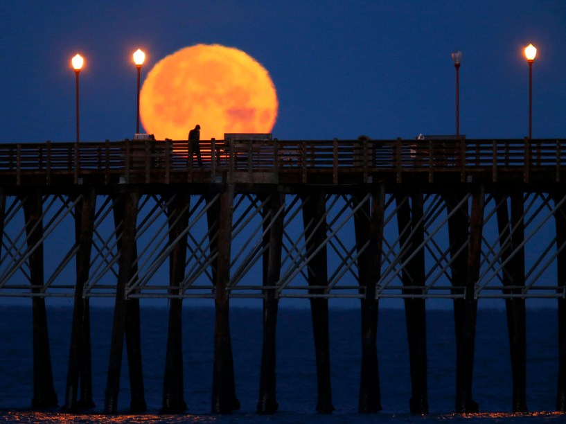 Homem caminha ao longo do cais com a lua ao fundo em Oceanside, na Califórnia - 05/03/2015