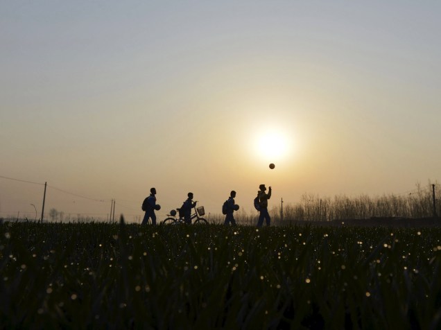 Estudantes brincam com bola de futebol no caminho para o Centro Primário da Cidade de Shunji, no condado de Xangai, China. Apesar da estrutura precária, os times masculinos e femininos da escola se destacam na competição municipal