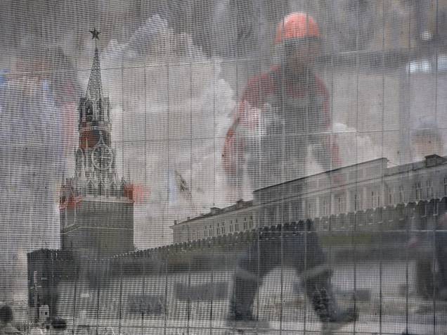 Trabalhador passa por trás de cerca transparente com imagem da Praça Vermelha, em uma construção em Moscou